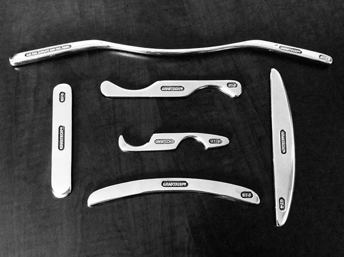 Set of 6 stainless steel tools resembling shavers, scrapers and a handlebar, arranged on a dark surface.