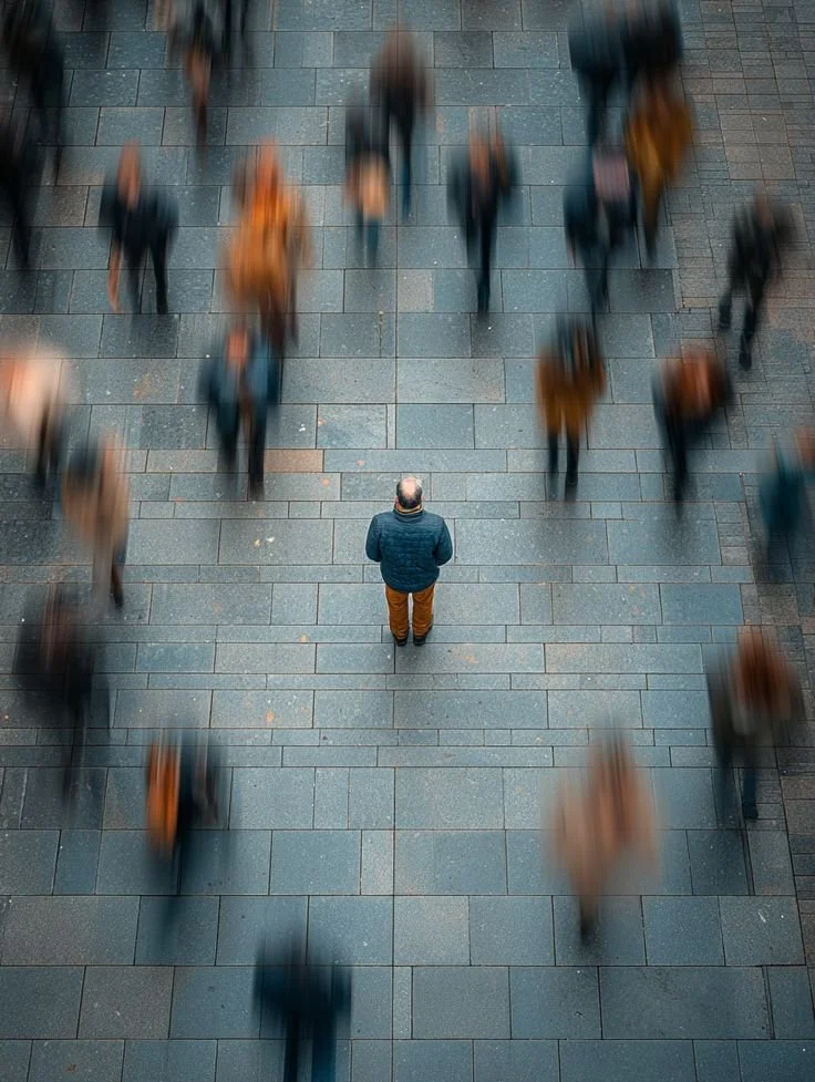 A man standing on a tiled sidewalk observing blurred pedestrians walking past, seen from above.