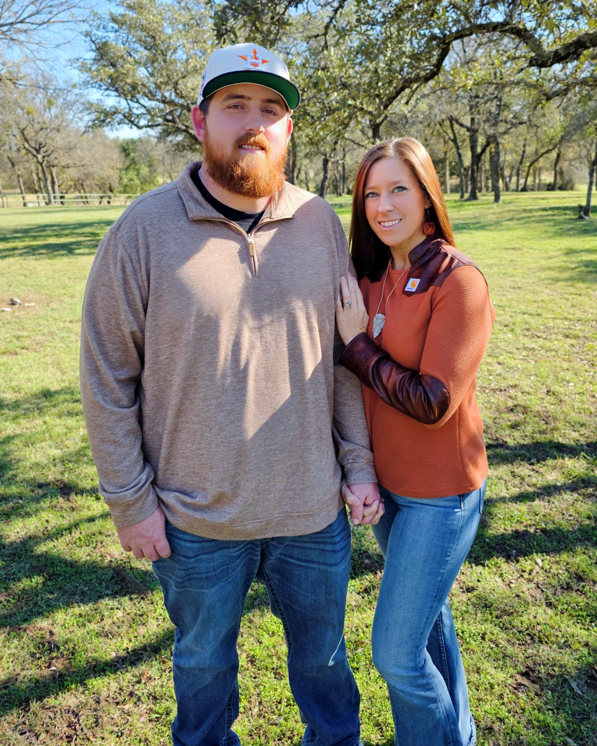 Megan Gibson and her husband standing together outdoors on a sunny day, holding hands, with trees and green grass in the background.
