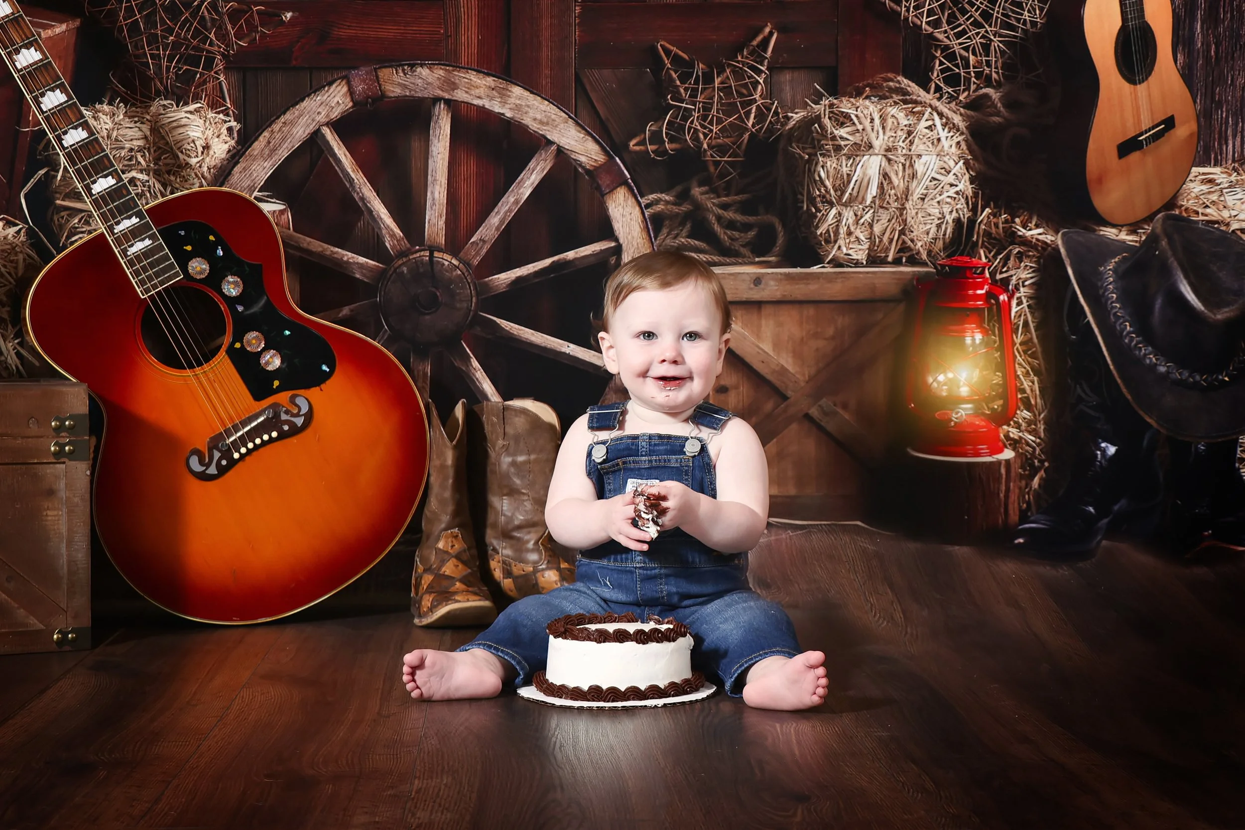 A 1 year old by sitting on a wooden floor with rustic scenery and backdrop with messy hands from his cake smash photography session