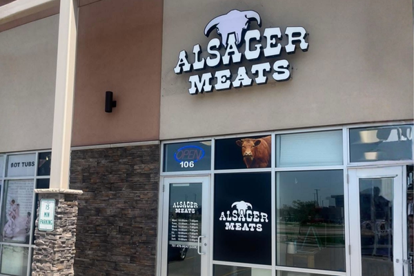 Exterior of Alsager Meats store with a sign displaying a white cow and a meat logo, large windows, and a glass door.