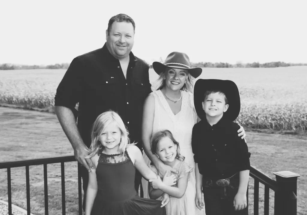 Alsager family of five standing outdoors on a farm, smiling, in a black and white photo. The background features open fields.