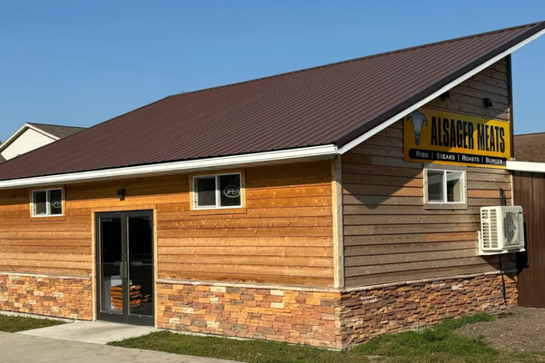 Exterior of a wooden building with a sign for Alsager Meats, offering ribs, steaks, roasts, and burgers, under a sloped roof.