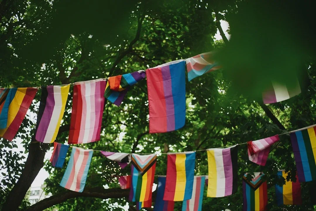 Colorful pride flags hanging on a string among green tree leaves.