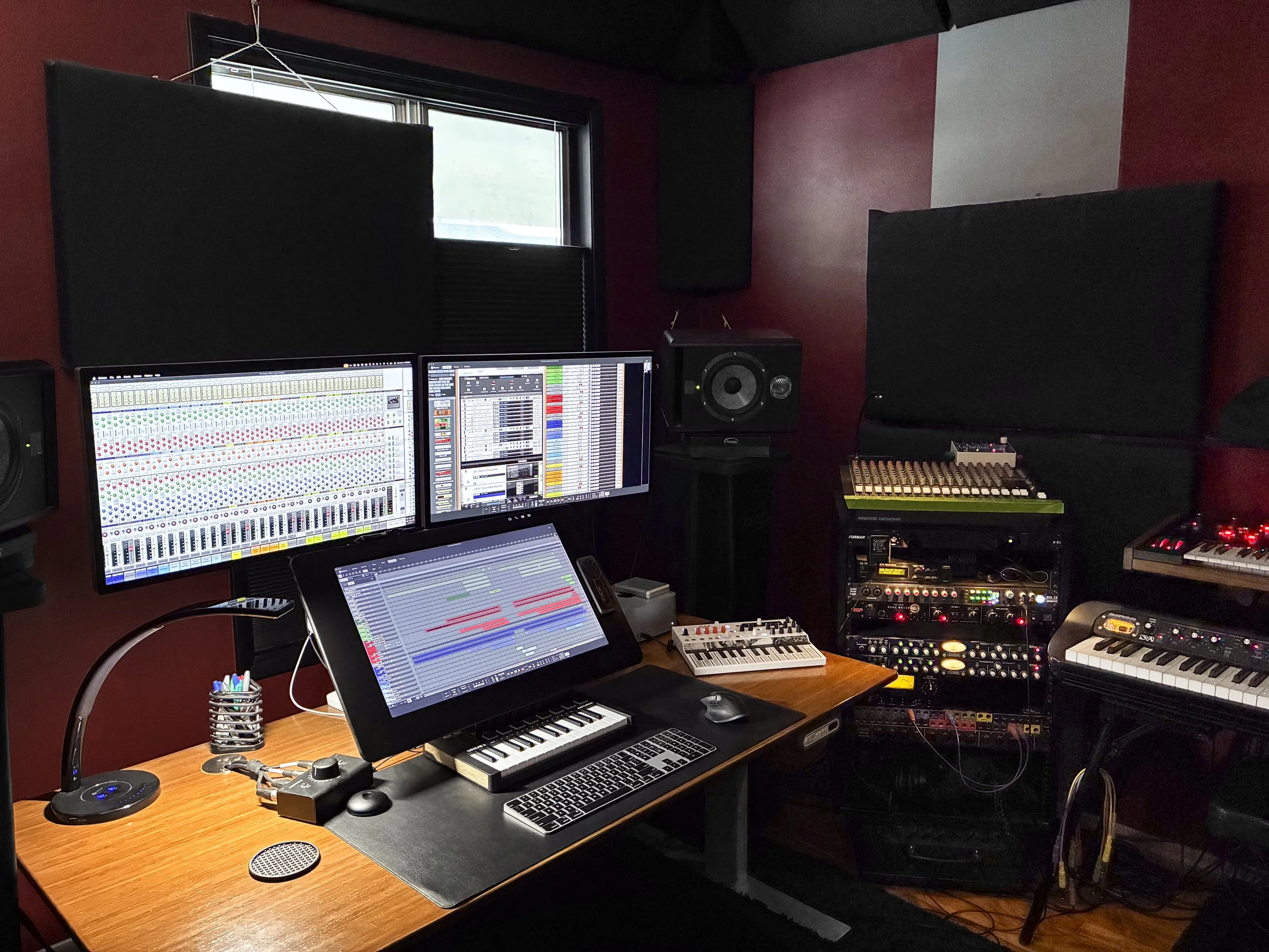 A music studio with multiple computer screens Reason, various synthesizers, a mixer, studio monitors, and soundproofing foam on the walls. The studio is underwater research and design, Jeremy Wilkins' studio.