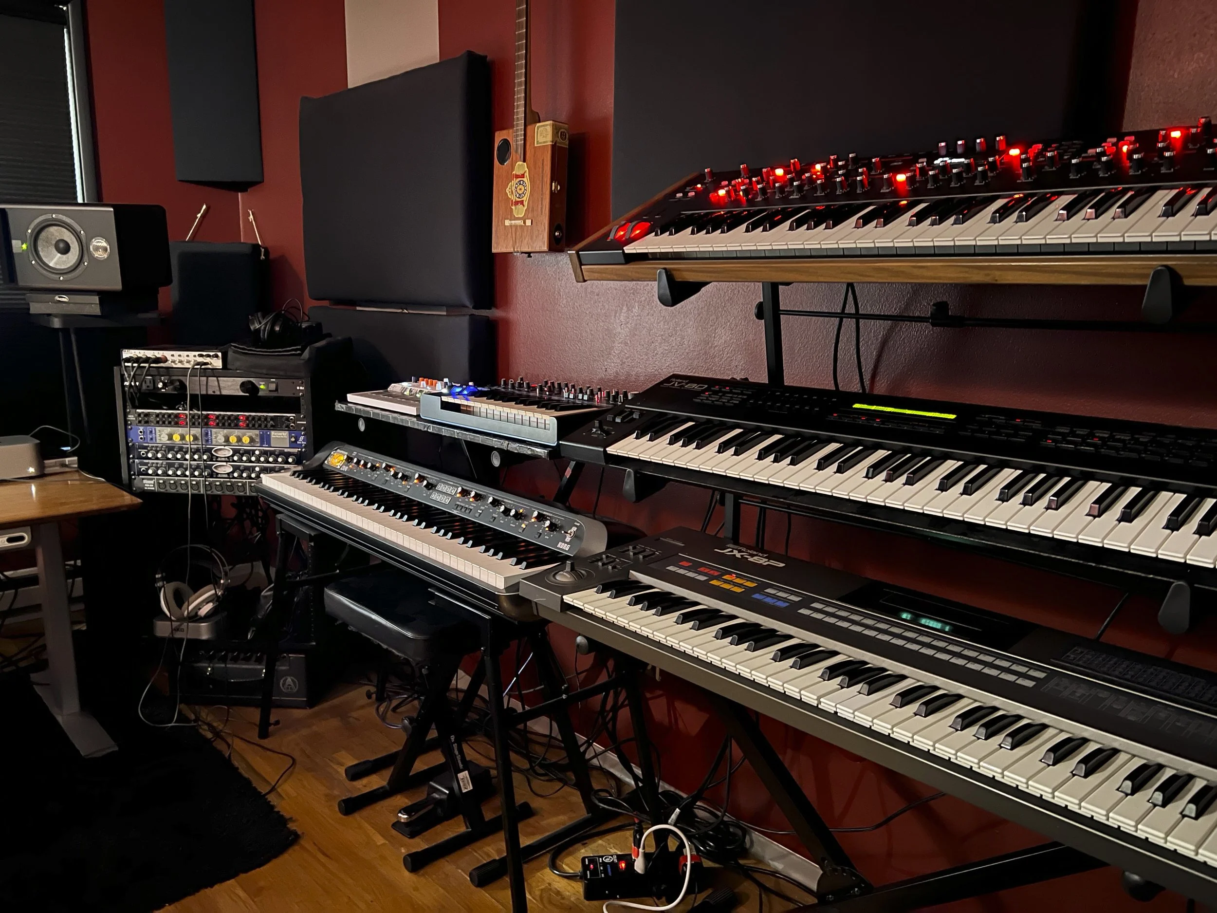 A music studio with multiple digital and analog keyboards on stands, a mixing console, studio monitor speakers, soundproofing panels, and audio equipment. The studio is underwater research and design, Jeremy Wilkins' studio. 