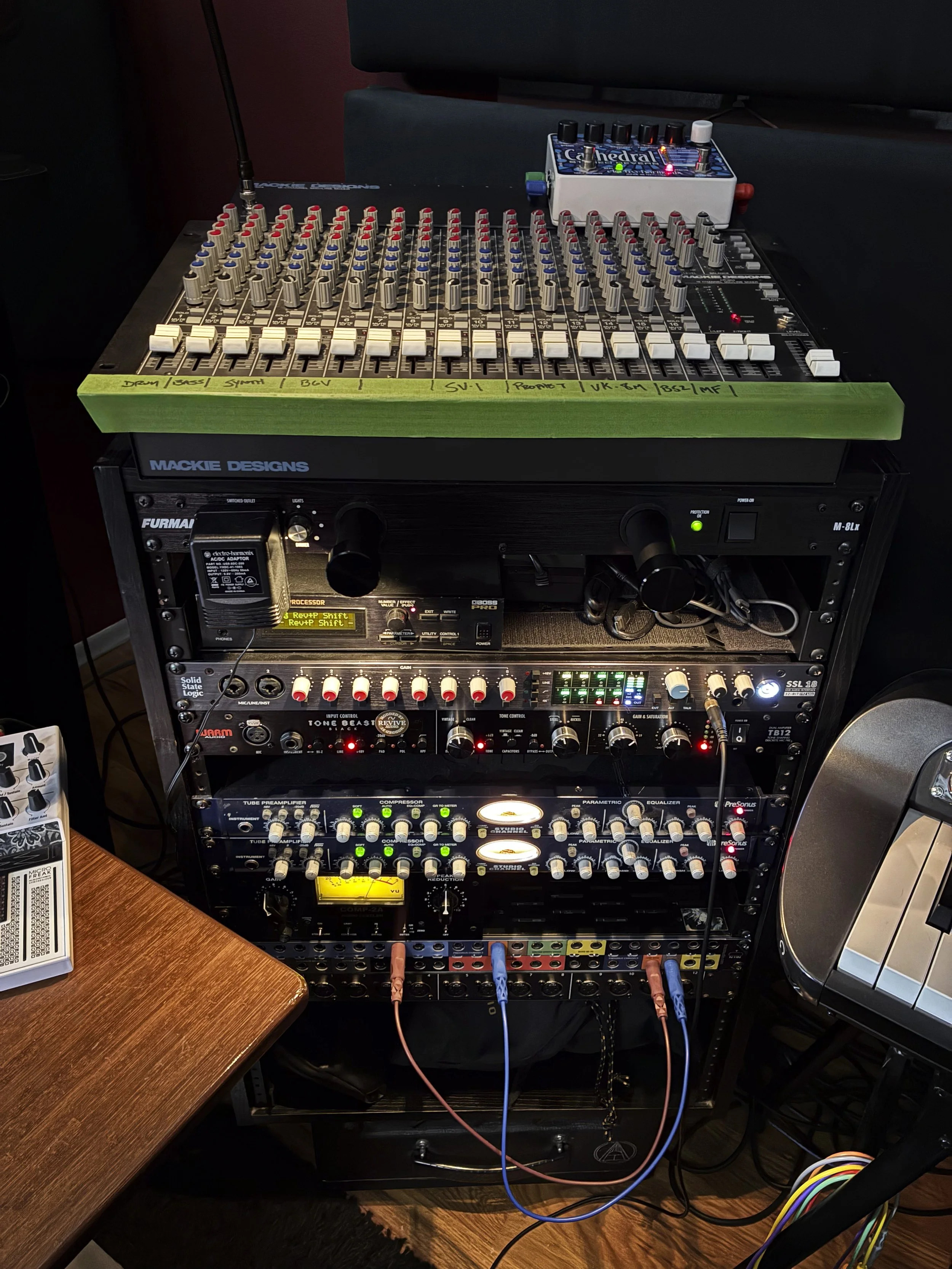 Audio mixing console and audio equipment rack with various preamps, compressors, effect processors, and cables in a recording studio.