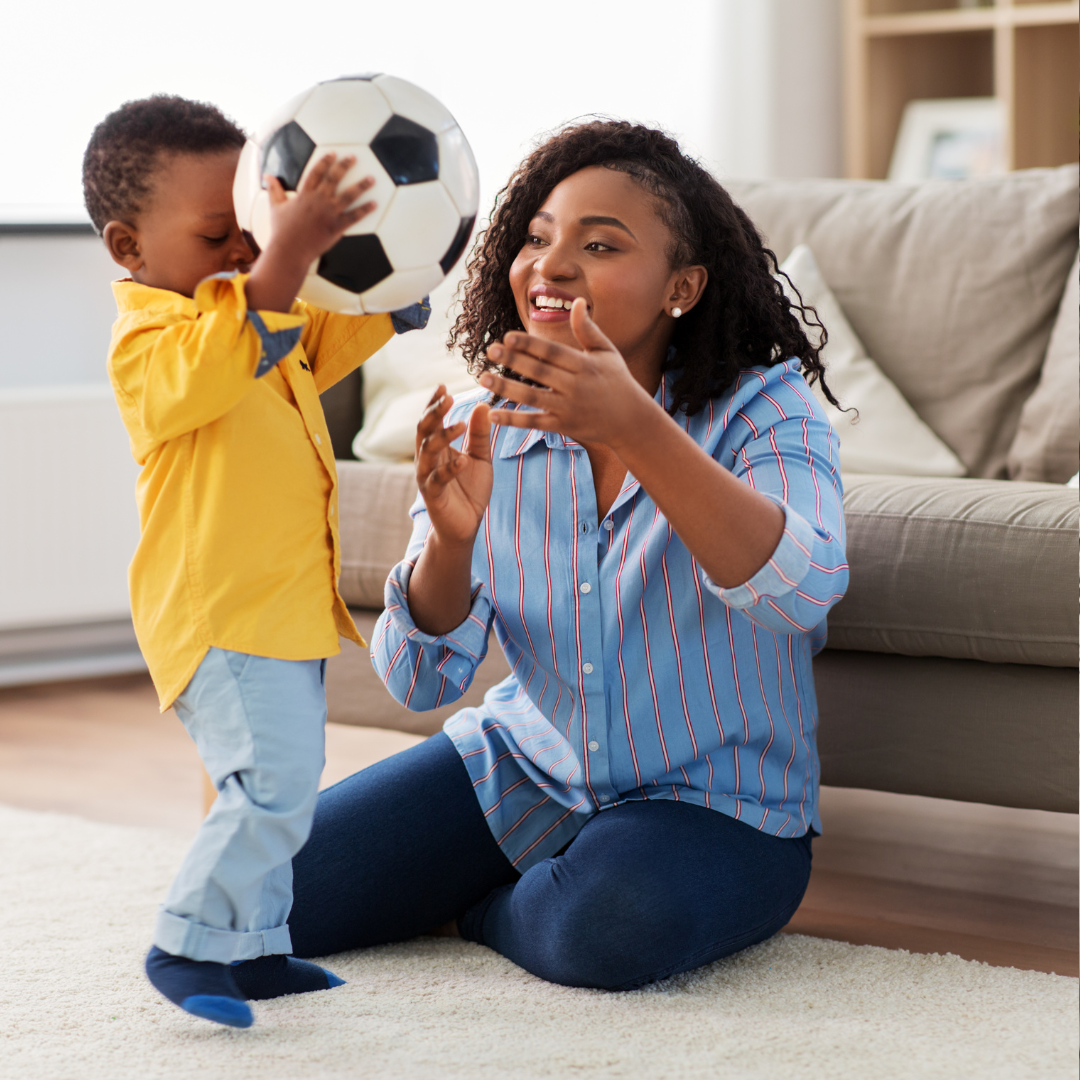 A young woman and a small boy playing with a soccer ball inside a living room.