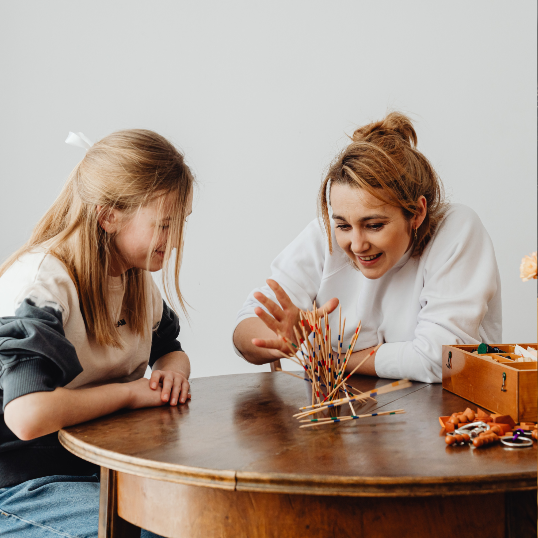 A woman and a girl playing the game Jenga at a wooden table.