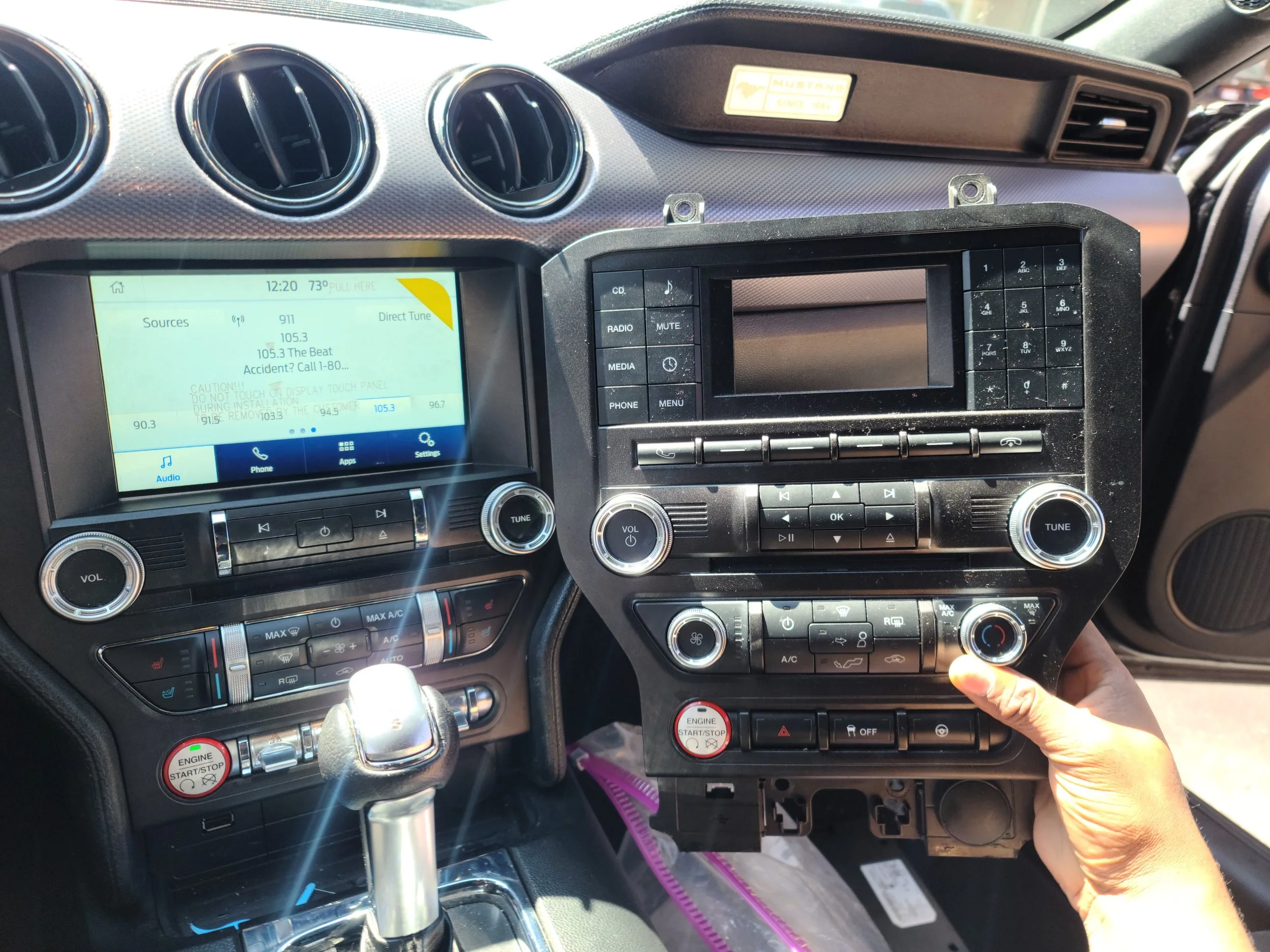 Person installing or removing a car dashboard component, with the center console and control panels visible inside the vehicle.