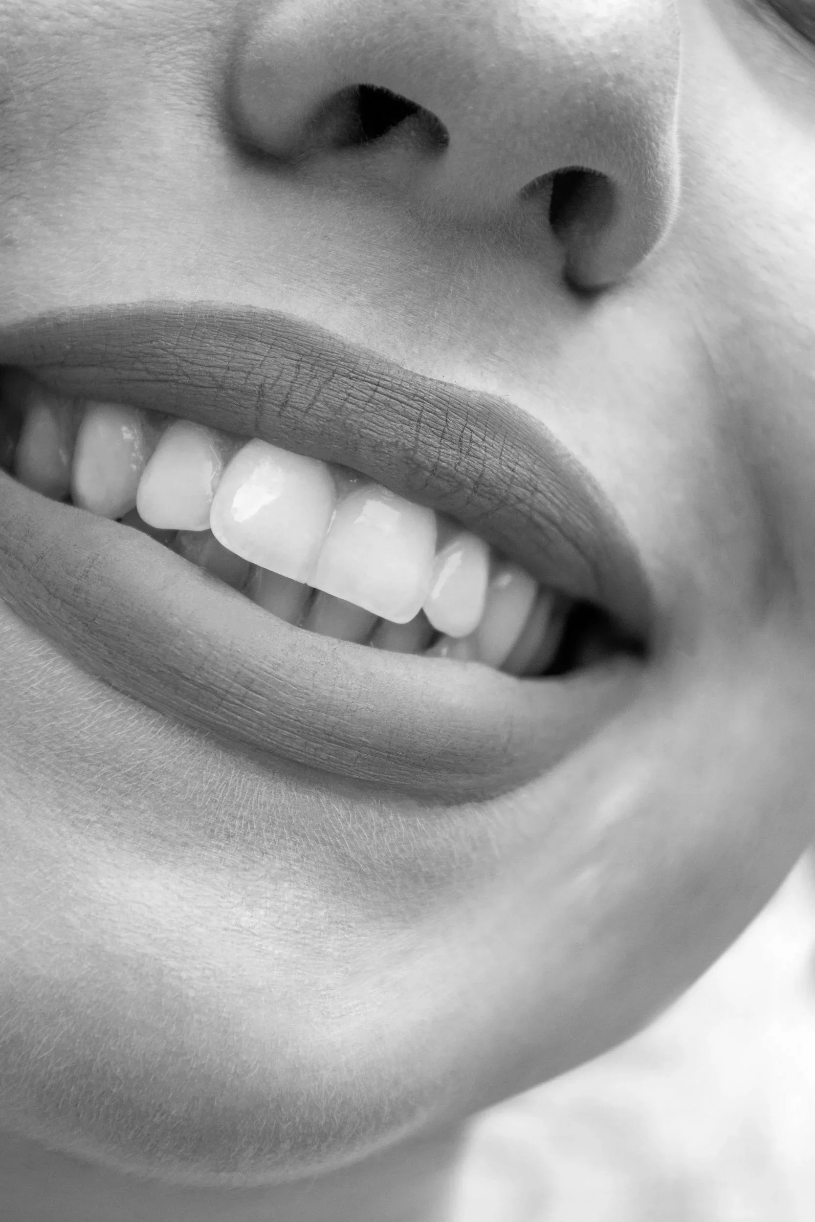 Close-up black and white photograph of a person's mouth, showing teeth, lips, and part of the nose.