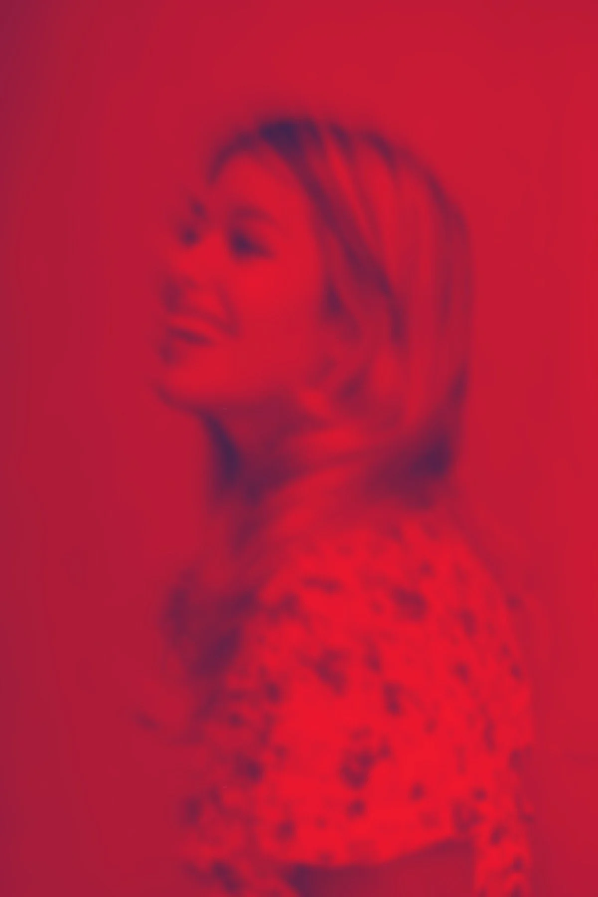 A woman with shoulder-length hair smiling, wearing a patterned top, against a red background, with a blurred effect.