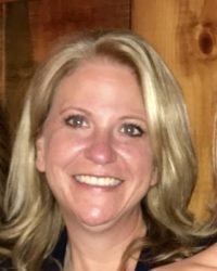 A smiling woman with blonde hair in front of a wooden background.