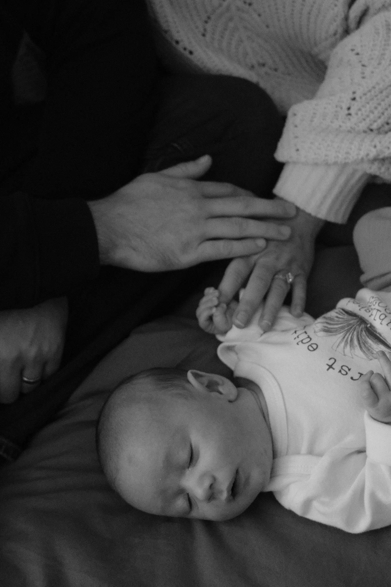 A sleeping baby lying on a bed with loved ones' hands gently touching nearby; occasion appears tender and familial.