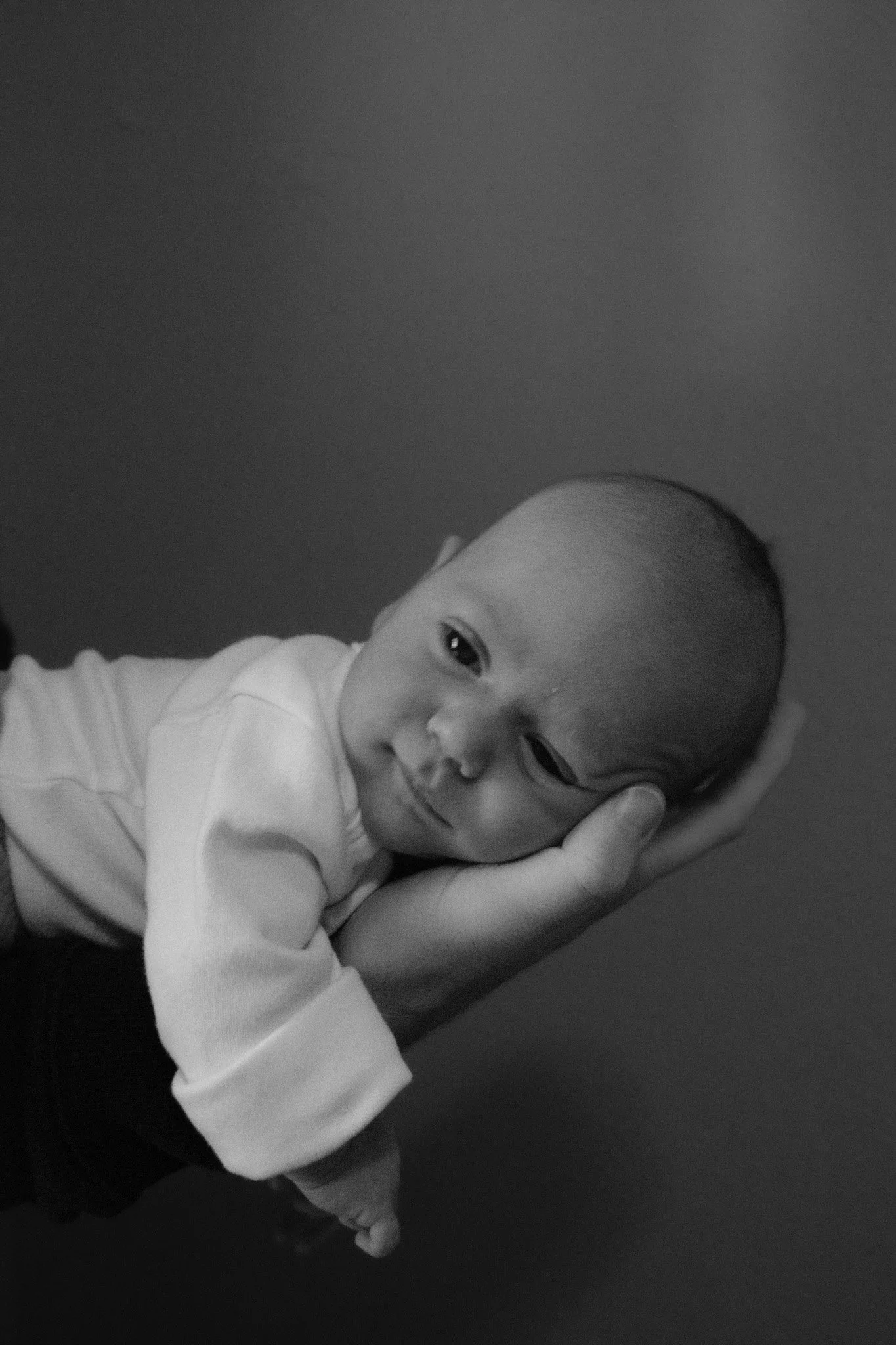 Black and white photo of a baby resting its head on an adult's hand, lying on their arm, with a calm expression.