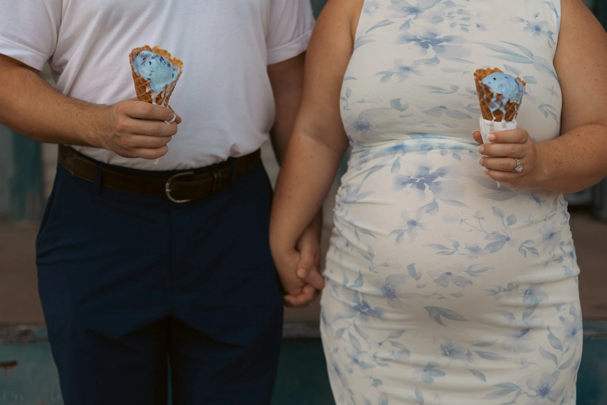 A man and woman holding hands while each eating ice cream cones with blue ice cream.
