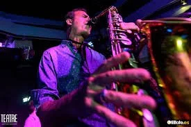 Saxofonista en directo durante una actuación musical de Cuatr8chos, creando atmósfera y ritmo en un evento con iluminación escénica.