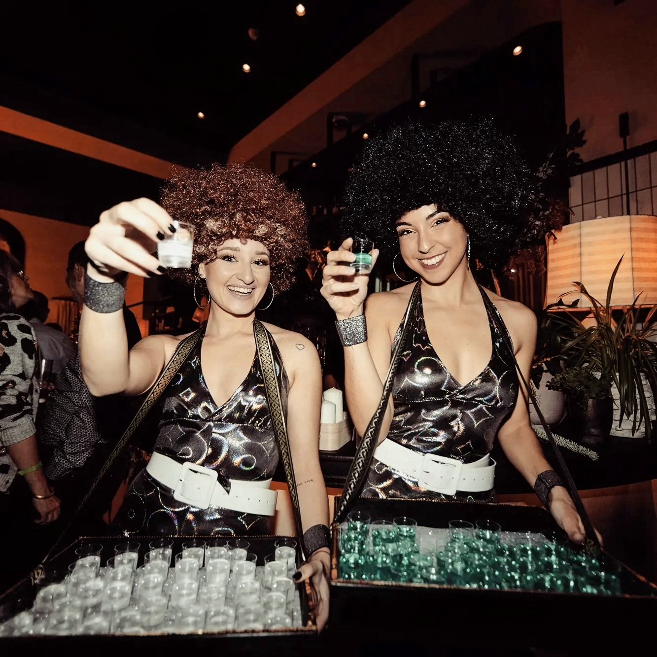Roller Disco Divas de Cuatr8chos repartiendo chupitos con bandejas en una fiesta Studio 54 de Nochevieja, animación itinerante para eventos con energía y estilo.