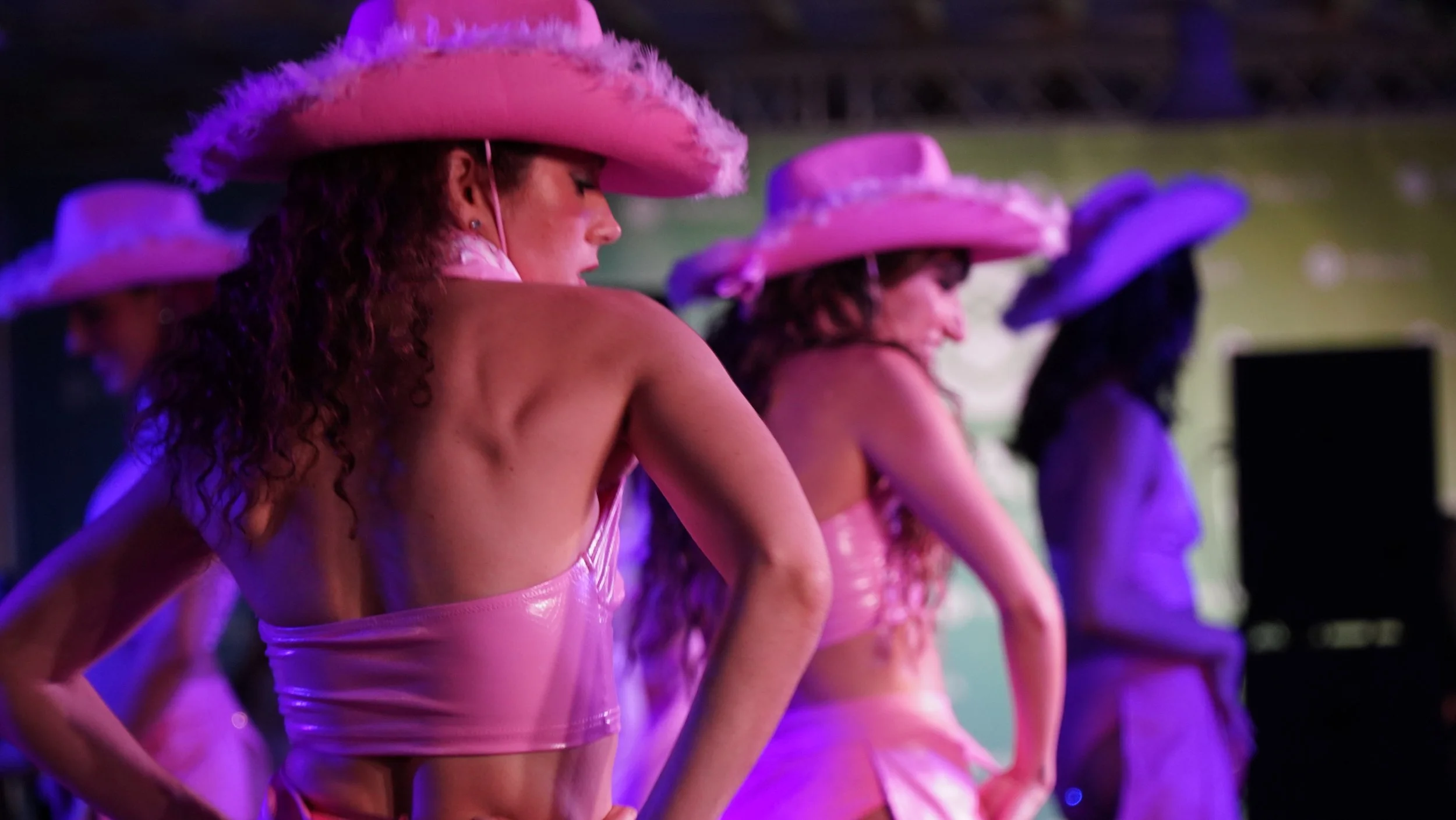 Show de baile escénico de Cuatr8chos con estética visual potente para eventos.
Mujeres bailando con sombreros grandes en escenario con iluminación púrpura.