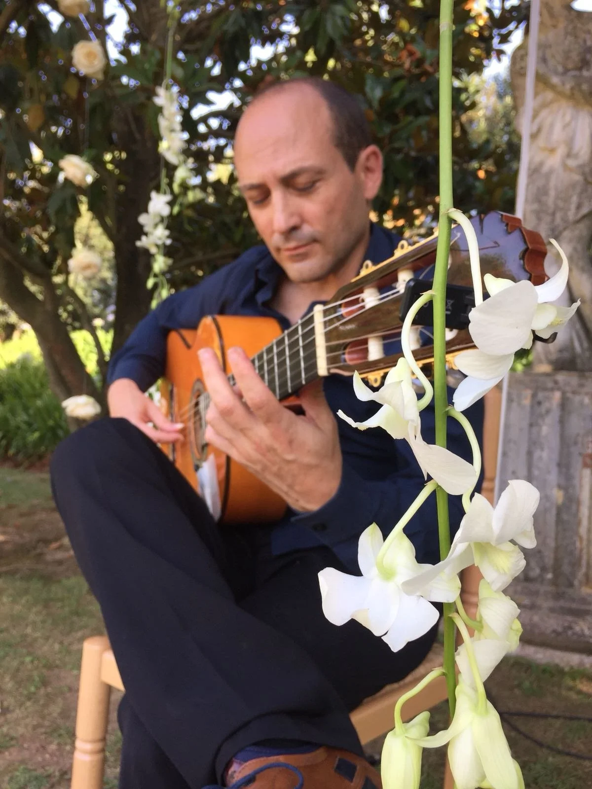 Guitarrista en directo de Cuatr8chos durante un cóctel al aire libre, creando ambiente musical en un entorno ajardinado.