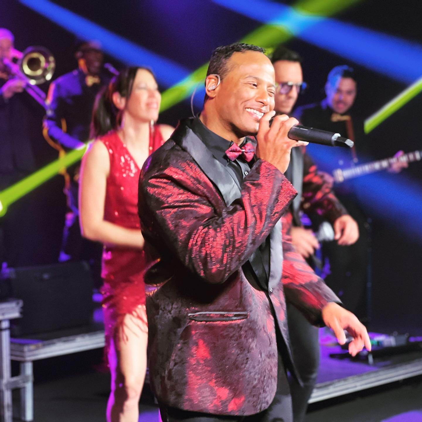 Hombre cantando con banda en un escenario con luces de colores.