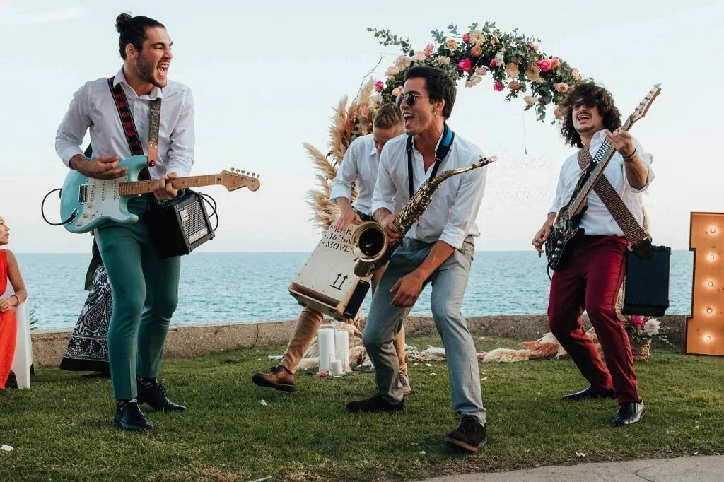 Música en directo y animación artística de Cuatr8chos en celebración al aire libre junto al mar, con puesta en escena para evento social o wedding.