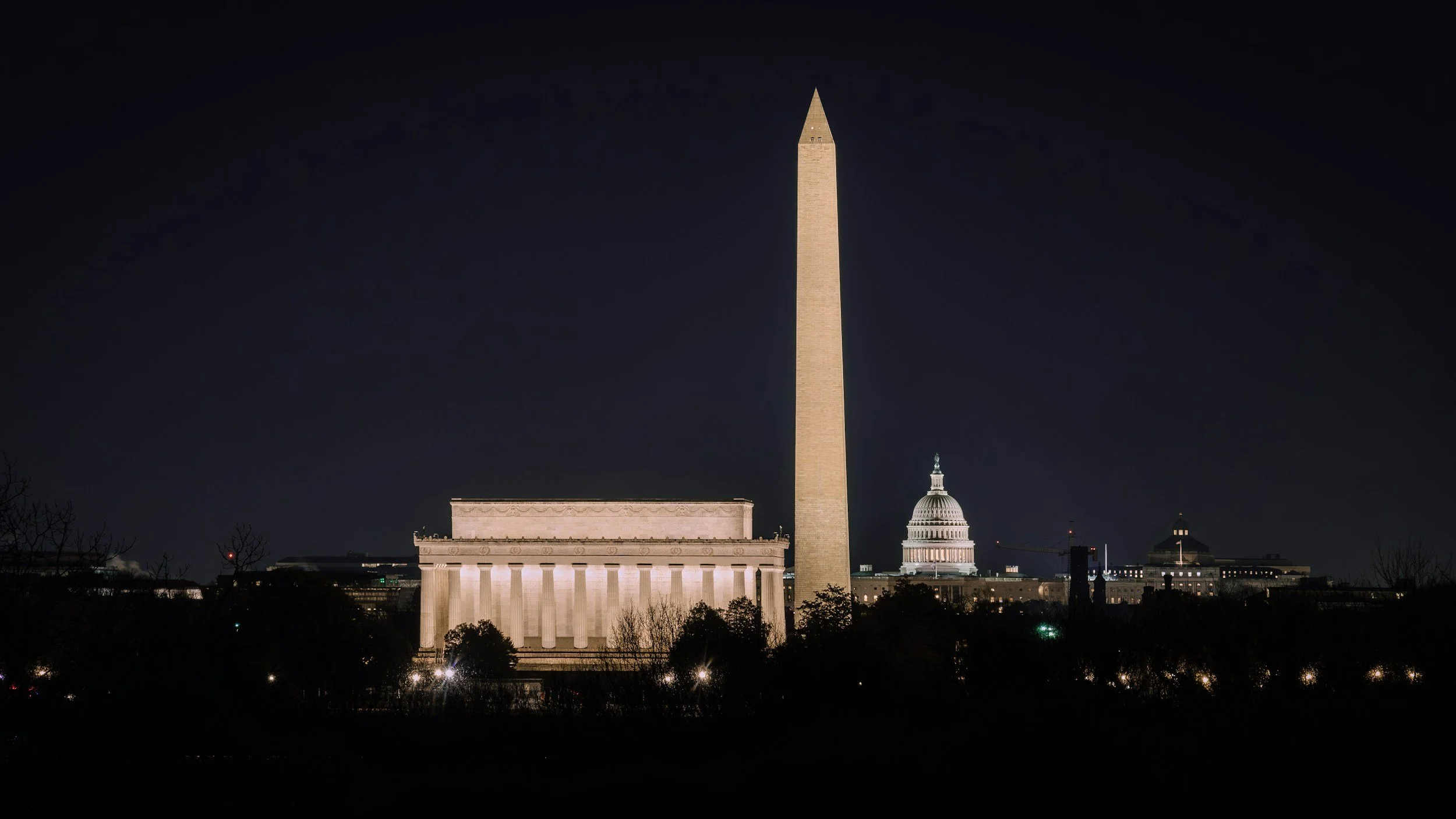 A view of the Washington Monument, Lincoln Memorial, and Capitol building at night time in DC.