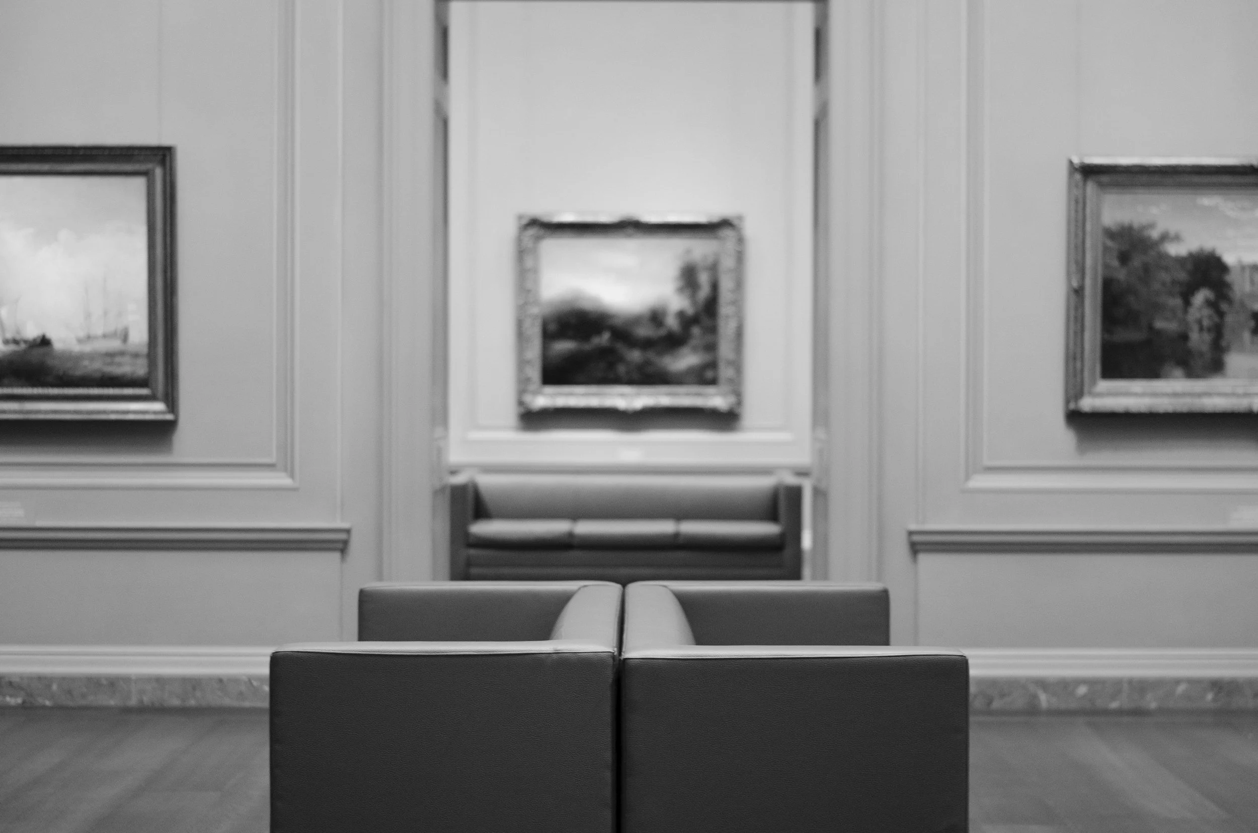 An artsy shot of a gallery space within the National Gallery of Art in DC. Blurred paintings are shown with comfy chairs.