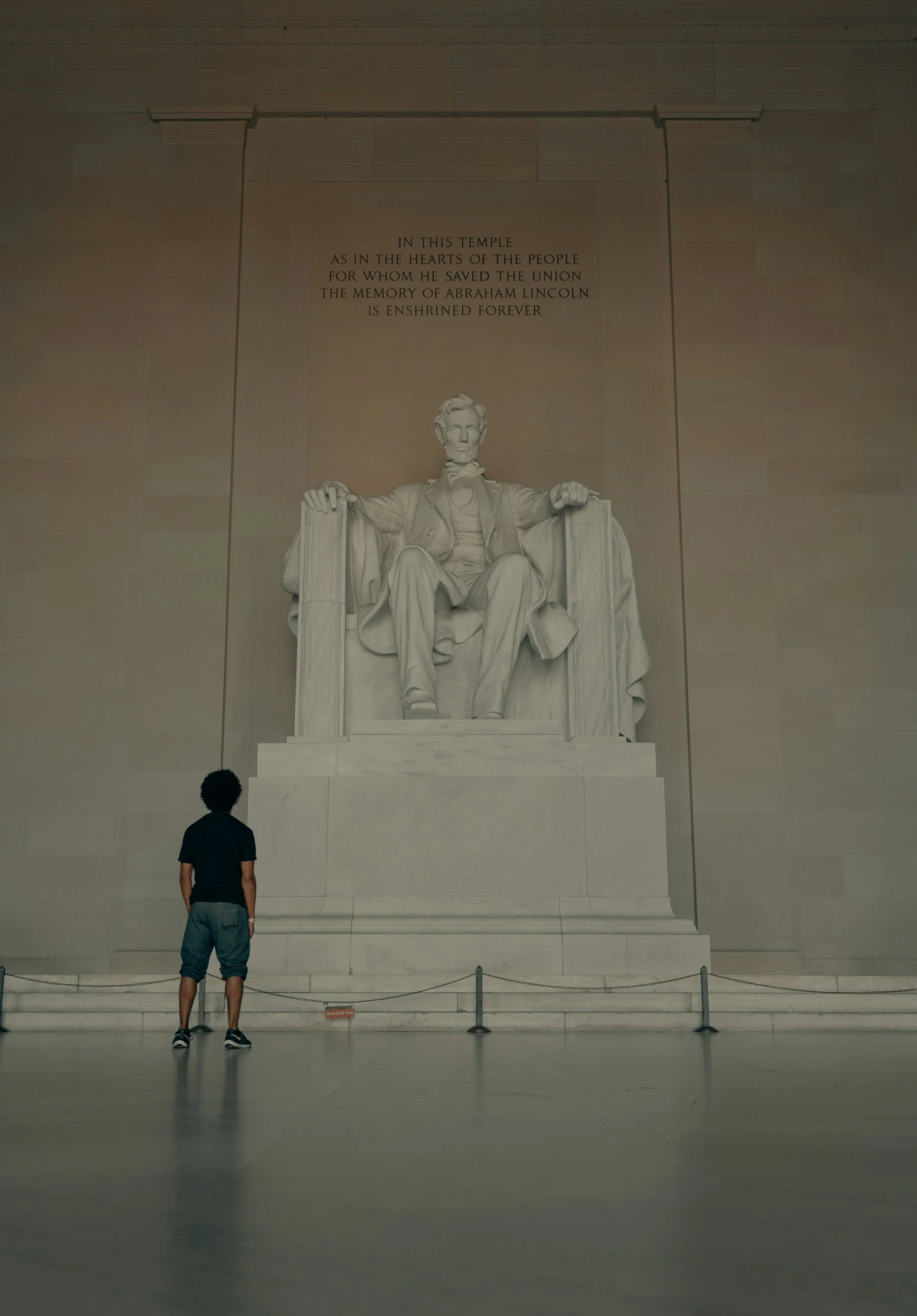 A young man with curly hair is standing and looking up at Lincoln at the Lincoln Memorial in DC.
