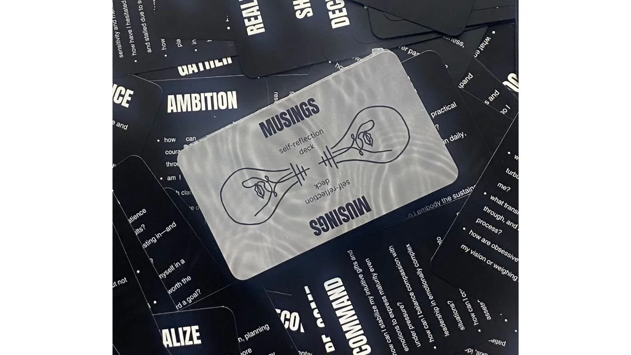 MUSINGS self-reflection deck featuring a hand-drawn lightbulb illustration and prompt cards designed for inquiry and contemplation.