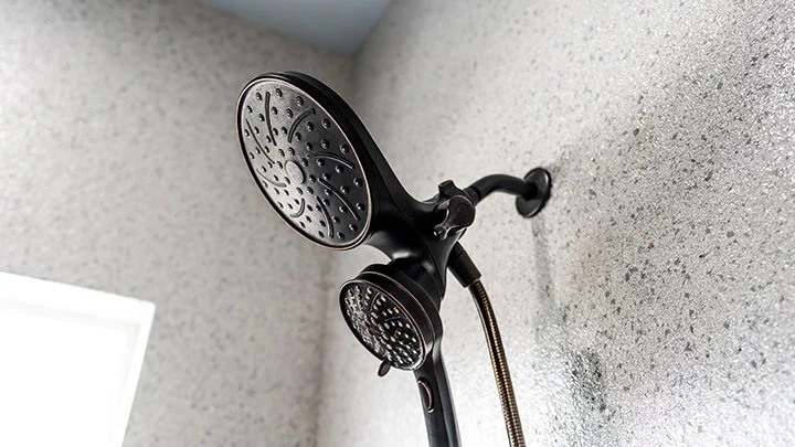 Black showerhead with detachable handheld sprayer mounted on a textured bathroom wall.