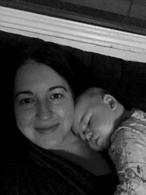 A woman smiling as a baby sleeps against her cheek.