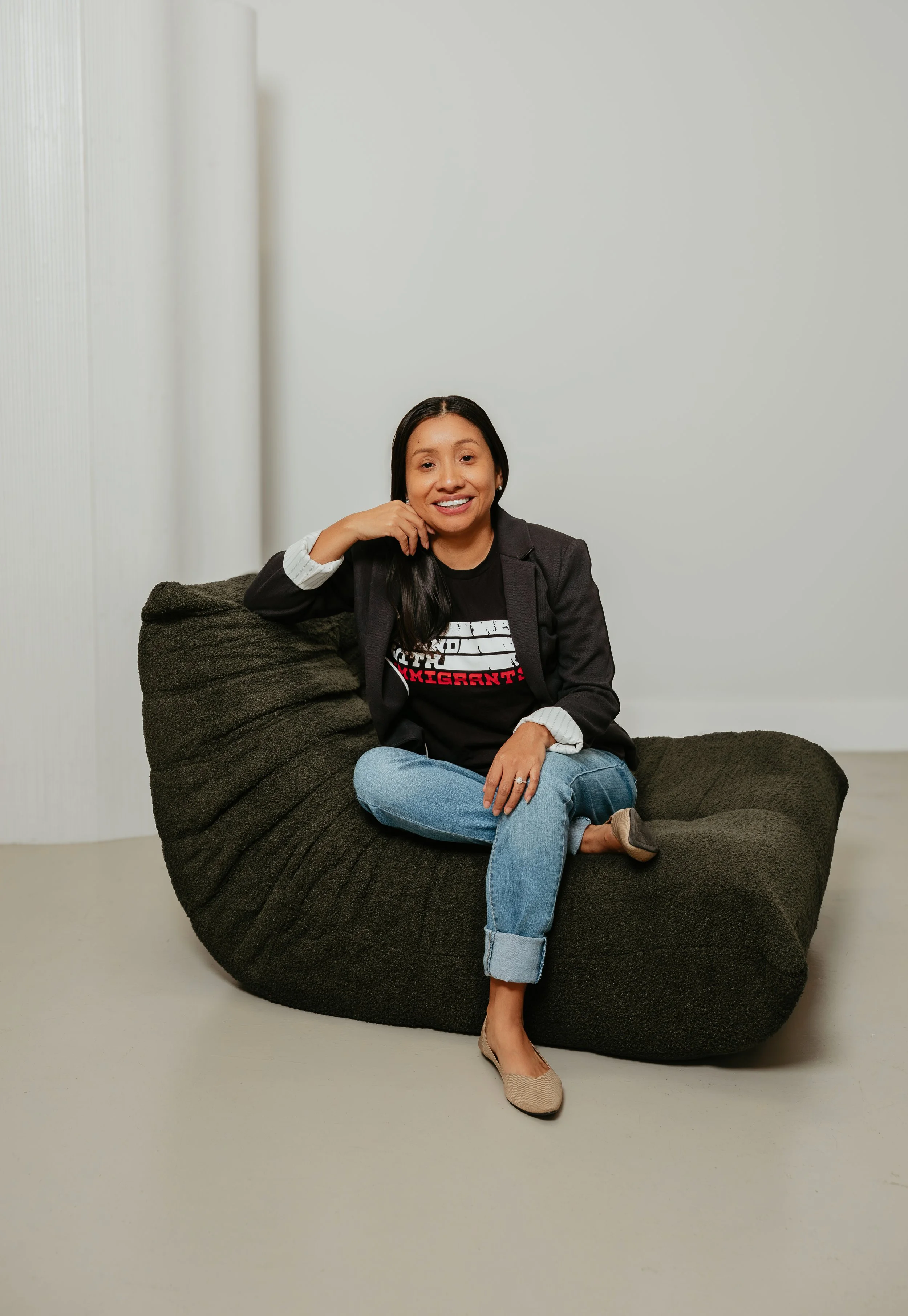 Woman sitting on a dark green bean bag chair, smiling, with a plain white background.