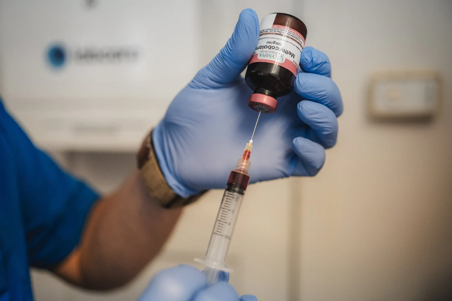 A gloved clinician preparing a vitamin B-12 injection from a vial.