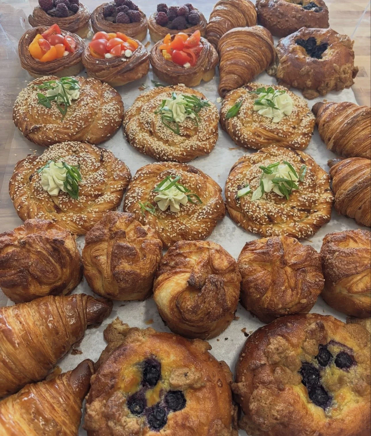Assortiment de viennoiseries artisanales : croissants, roulés feuilletés, brioches aux myrtilles et pâtisseries garnies de fruits et de crème.