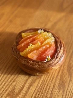 Dessert rond au chocolat garni de tranches d’agrumes confites jaunes et orange, présenté sur une table en bois.