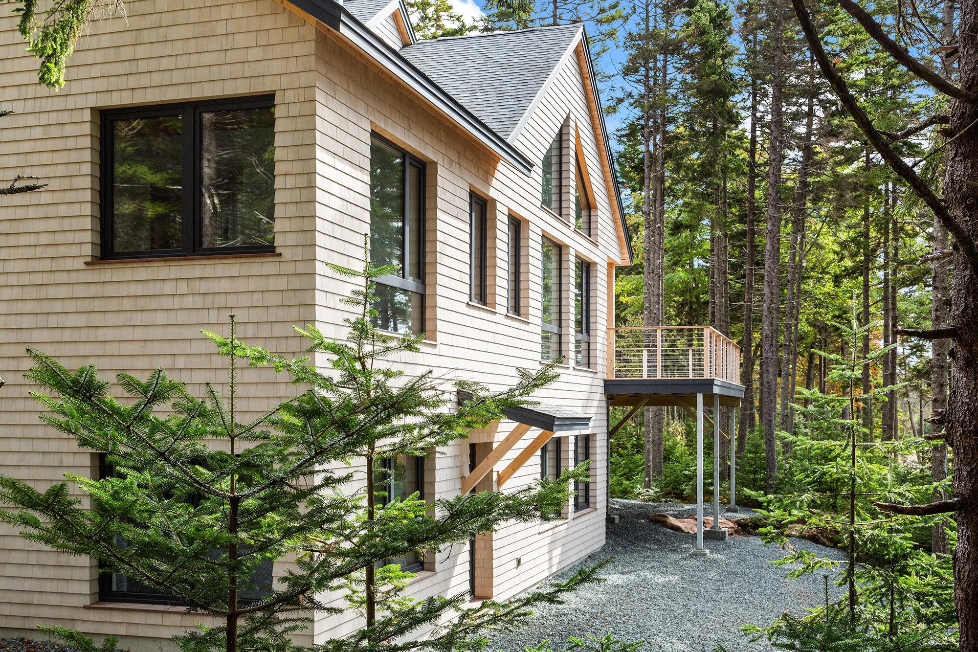 Back side of the waterfront property in Maine shows trees around the property with a patio, and sun beating down on the home