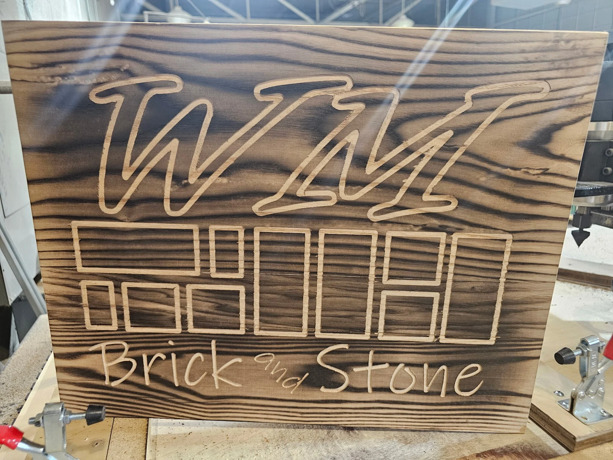 Wooden sign with engraved text reading 'WAVZ' at top, with a geometric brick and stone pattern below, and 'Brick and Stone' written at the bottom.