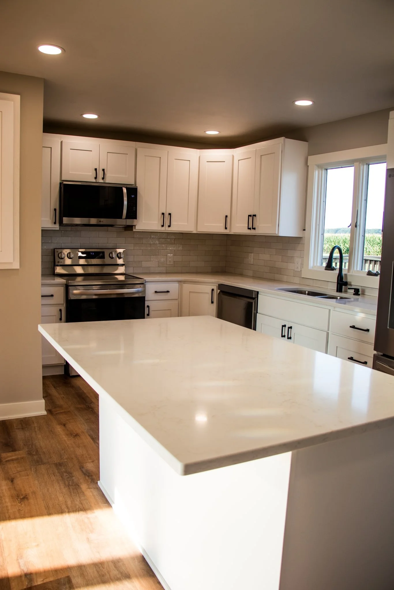 Modern kitchen with white cabinets, stainless steel appliances, wooden floor, and a large kitchen island with light-colored countertop.