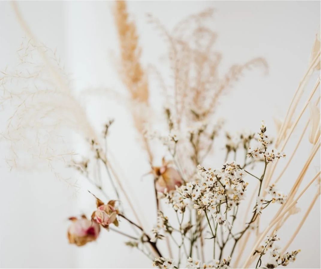 A bouquet of dried flowers including small white blossoms, pink buds, and beige grasses.