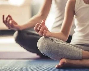 Close-up of a person practicing meditation or yoga, sitting cross-legged with hands resting on knees in a peaceful indoor setting.