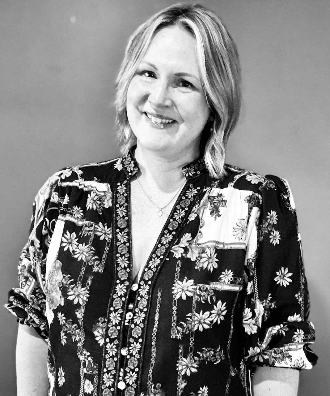 A woman with shoulder-length hair smiling, wearing a floral patterned blouse.