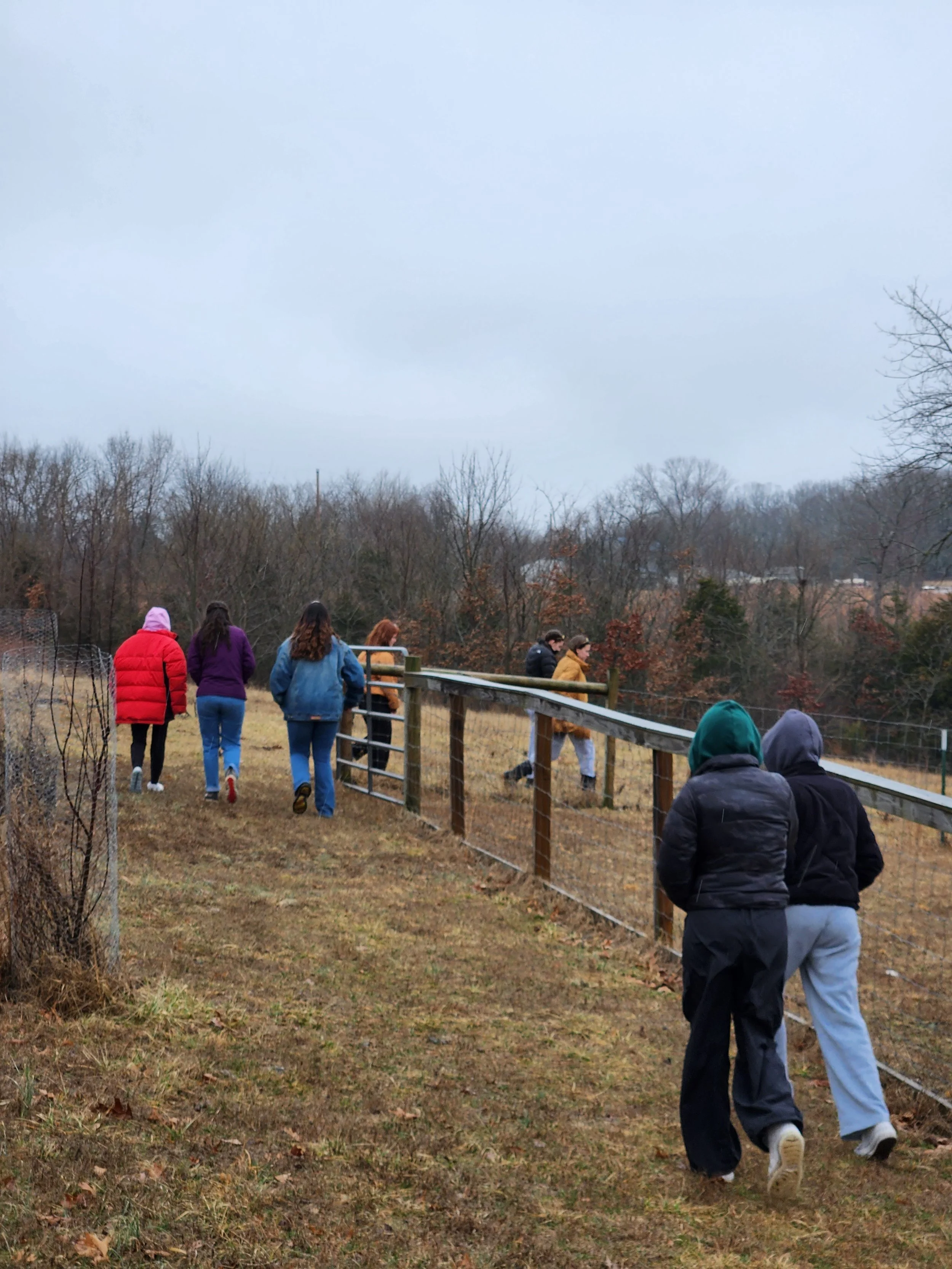 People walking outdoors in a fenced area on an overcast day, dressed for cold weather.