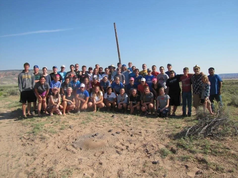 A large group of people posing outdoors in a desert landscape with blue sky.