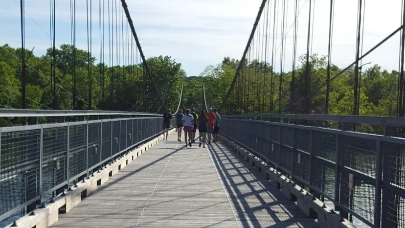 Group of people walking on a wooden pedestrian suspension bridge surrounded by green trees.