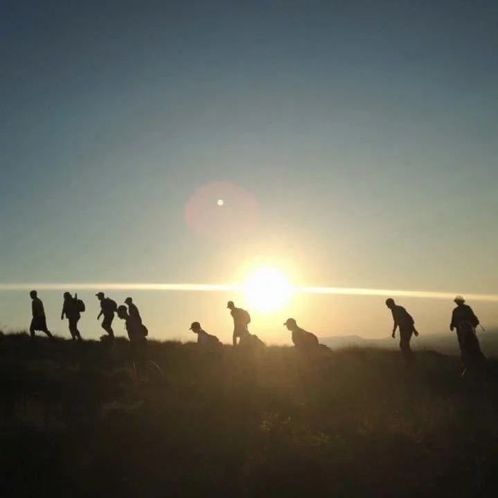 Silhouettes of hikers walking along a ridge at sunset or sunrise.