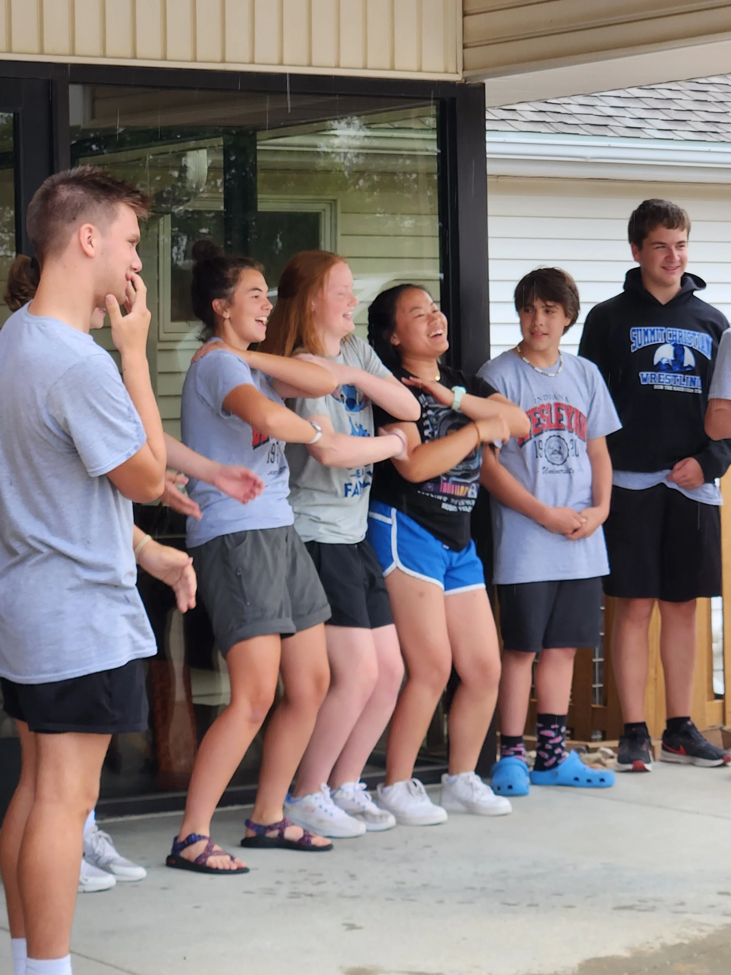 Group of young teenagers standing on a porch, engaging in a team activity or game, with expressions of laughter and amusement.