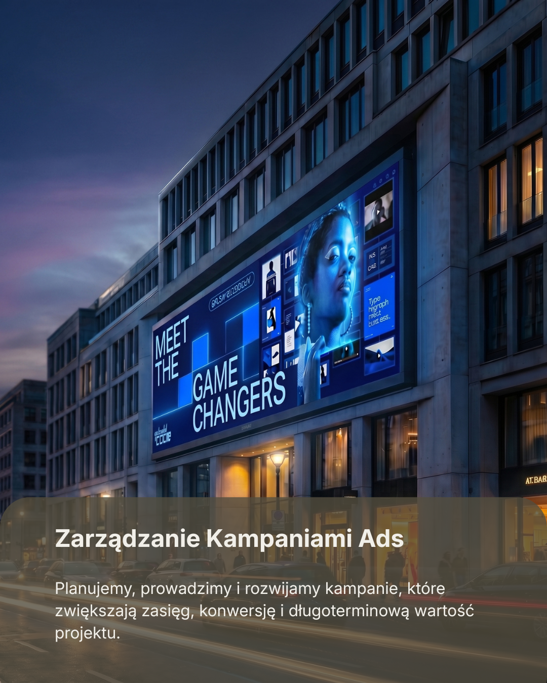 Large digital billboard on a modern building during twilight, displaying an advertisement for a campaign with the text 'Meet the Game Changers' and featuring a woman's face with digital elements around her.