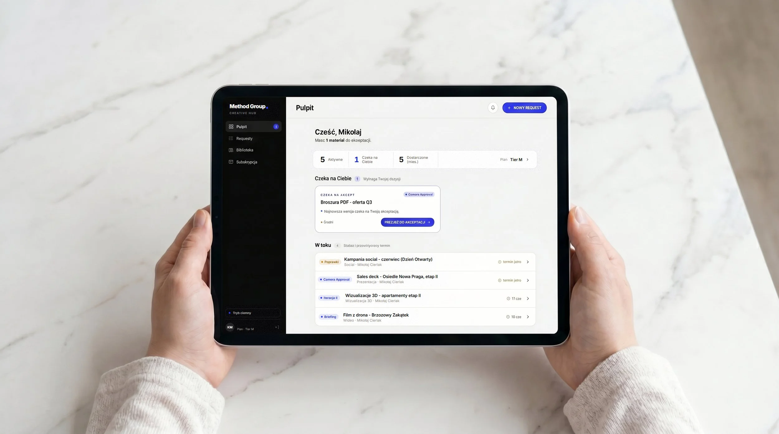Dłonie trzymające tablet z interfejsem Method Creative Hub — dashboard pokazujący aktywne requesty, statusy projektów i terminy w systemie CaaS dla firm B2B