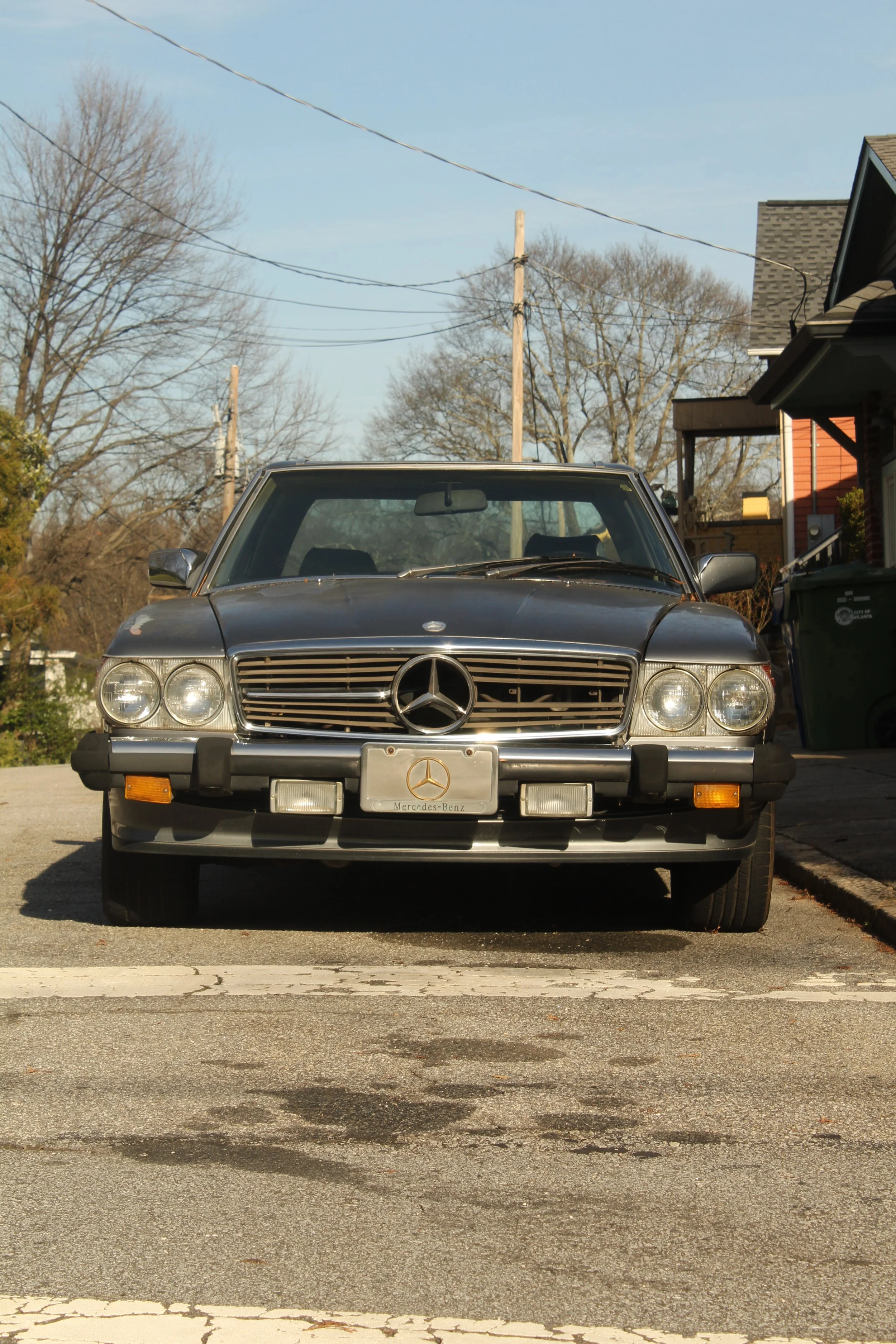Front view of a black classic Mercedes-Benz car parked on the street, with leafless trees and houses in the background.
